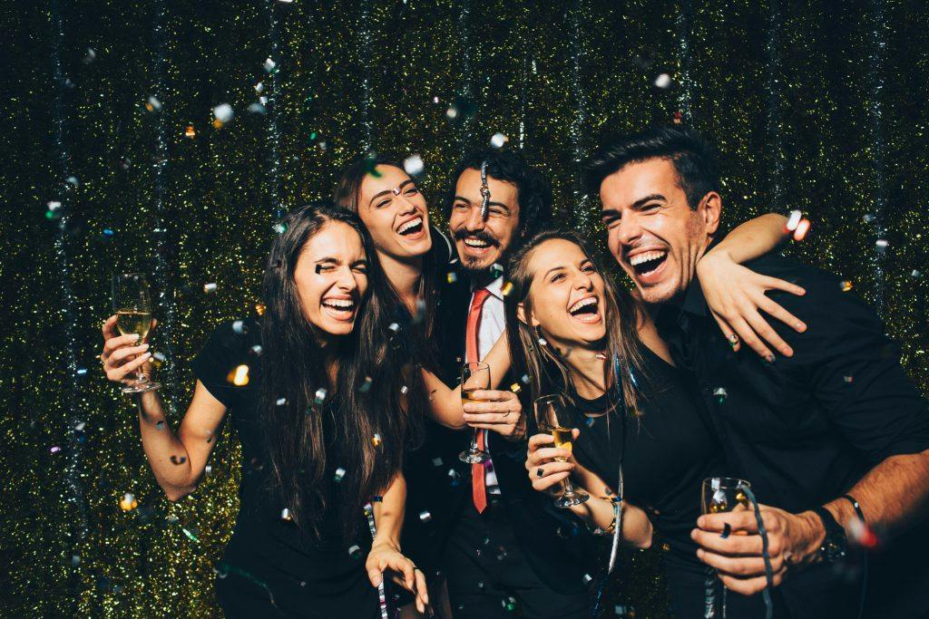 Group of friends laughing and celebrating with drinks and confetti.