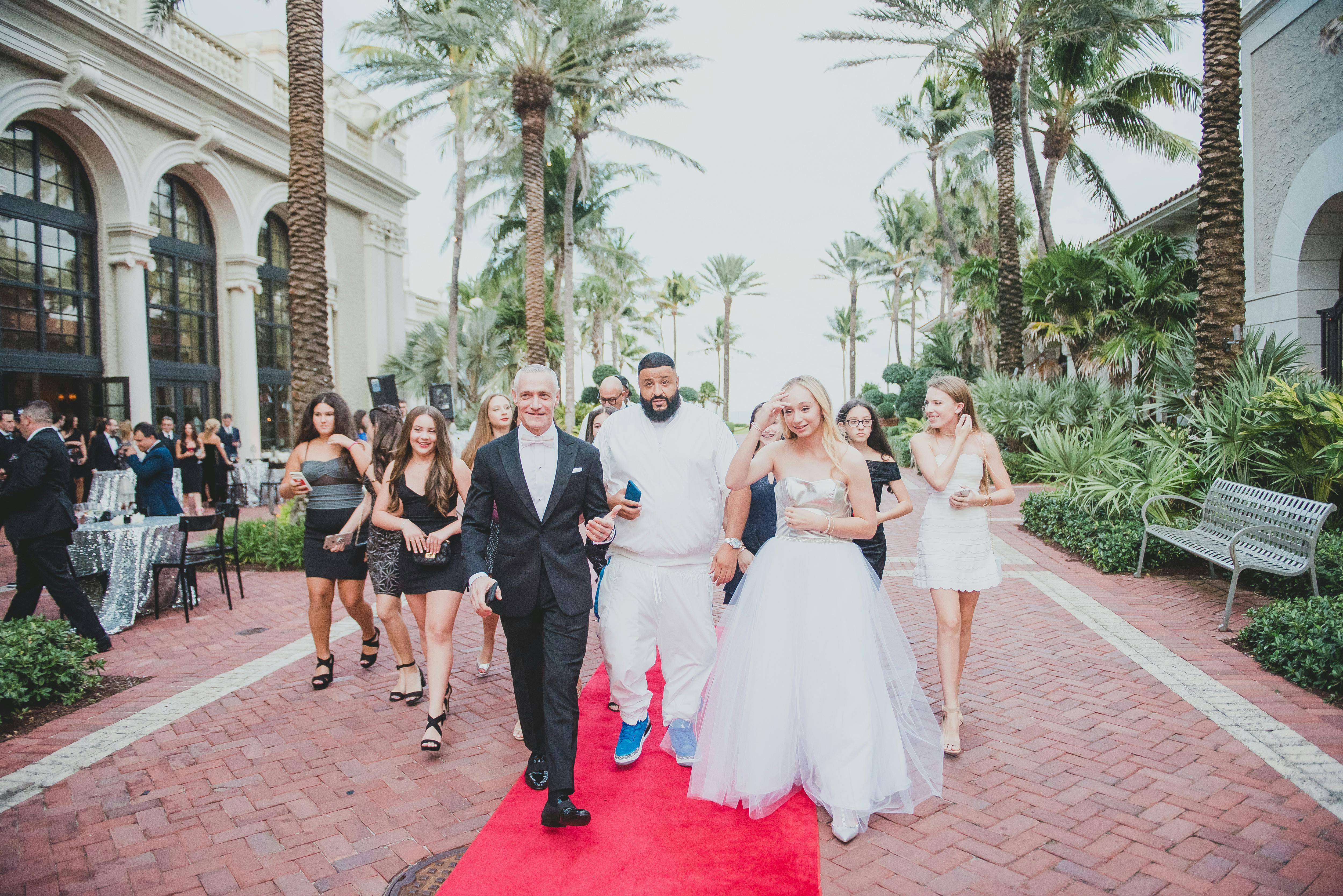 DJ Khaled and a bride walk down a red carpet with people around them