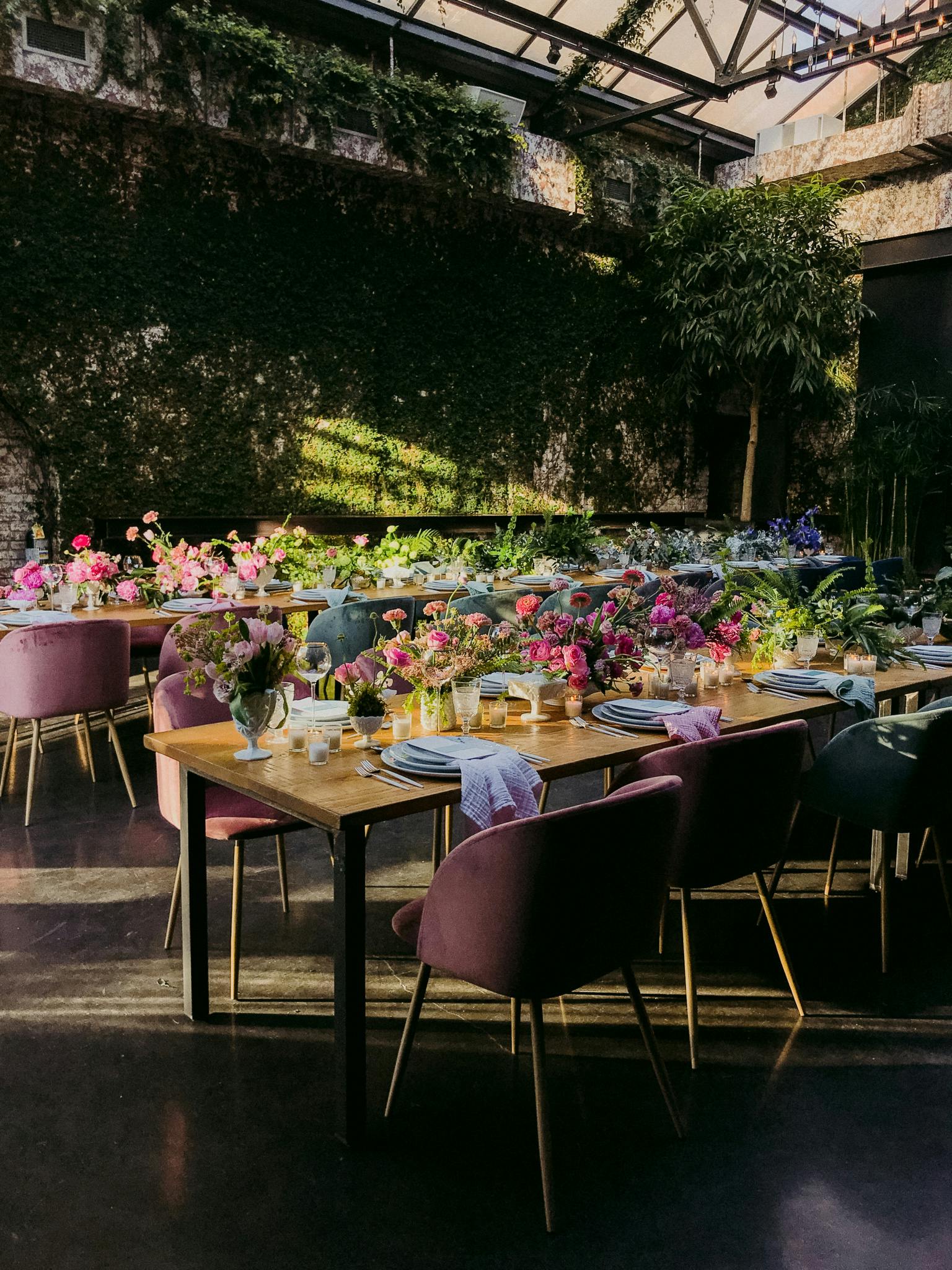 Greenhouse venue with plush purple chairs and bright colorful floral centerpieces atop long tables | PartySlate