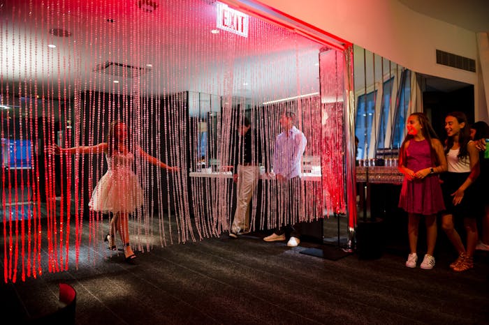 a girl comes through red tinsel to her friends on the other side. Arcade games are along the perimeter.