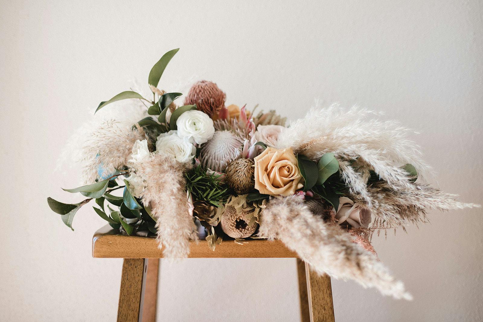 A wooden stool holds a feathery and pink bouquet of florals with a cool white backdrop.