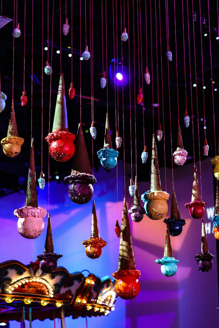 Ice cream scoop sculptures handing from red thread from ceiling at purple lit event | PartySlate