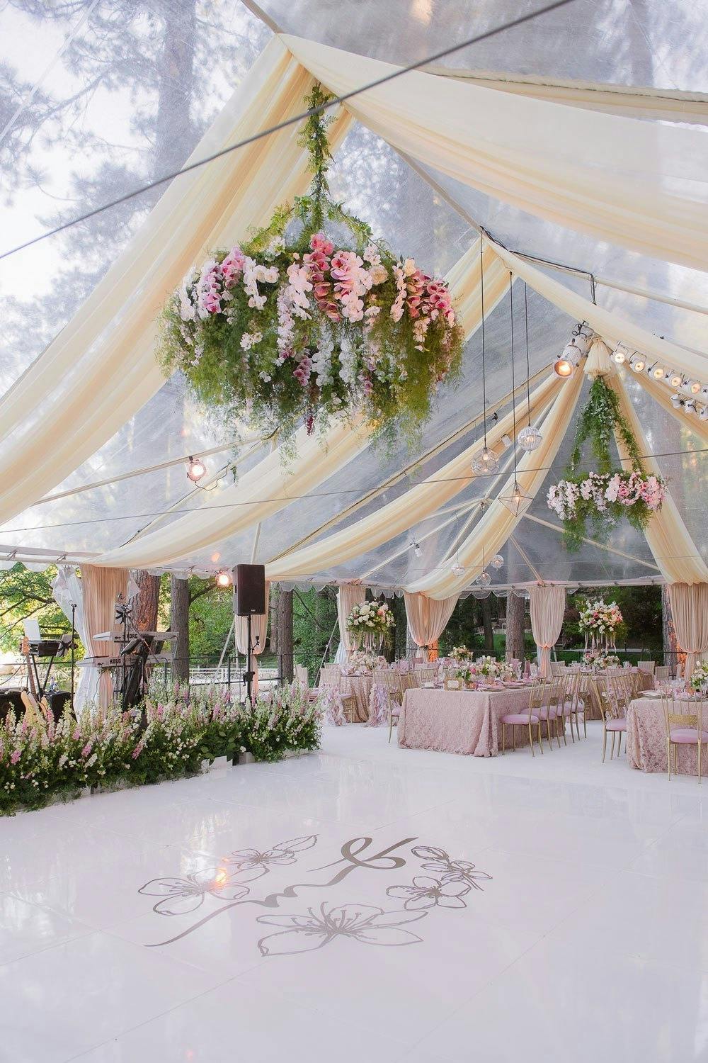 clear tent with gauzy draping and pink and green florals over dance floor