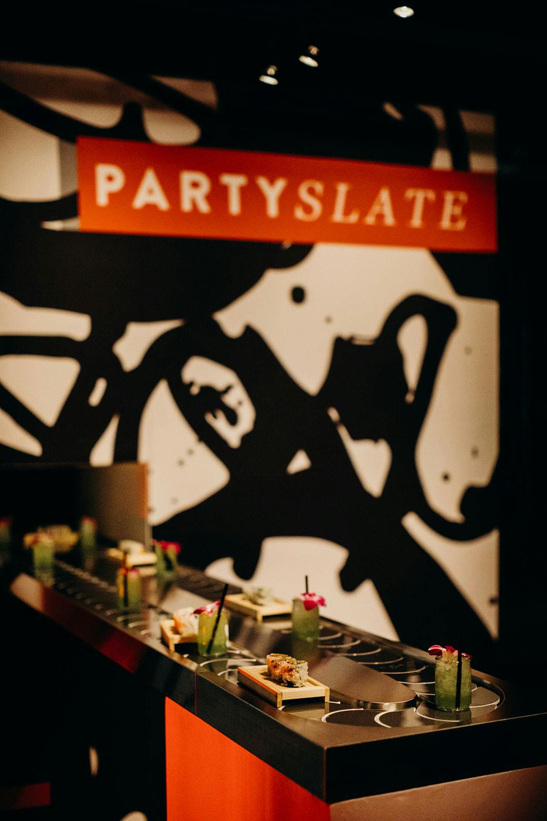 a 'U' shaped conveyer belt holds green drinks and plates of sushi. Red, white and black branding is in the background .