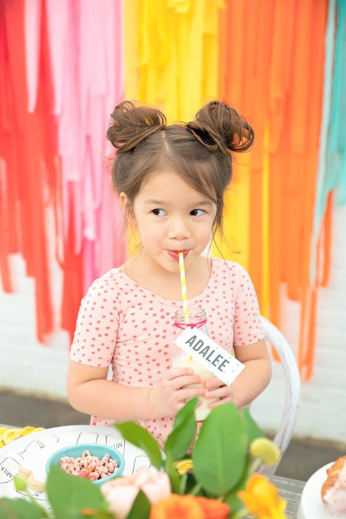 Girl sipping drink with her name on it with colorful tassels in the background | PartySlate