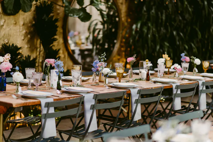 A long table with minimal floral arrangements. White linens hang off the edge.