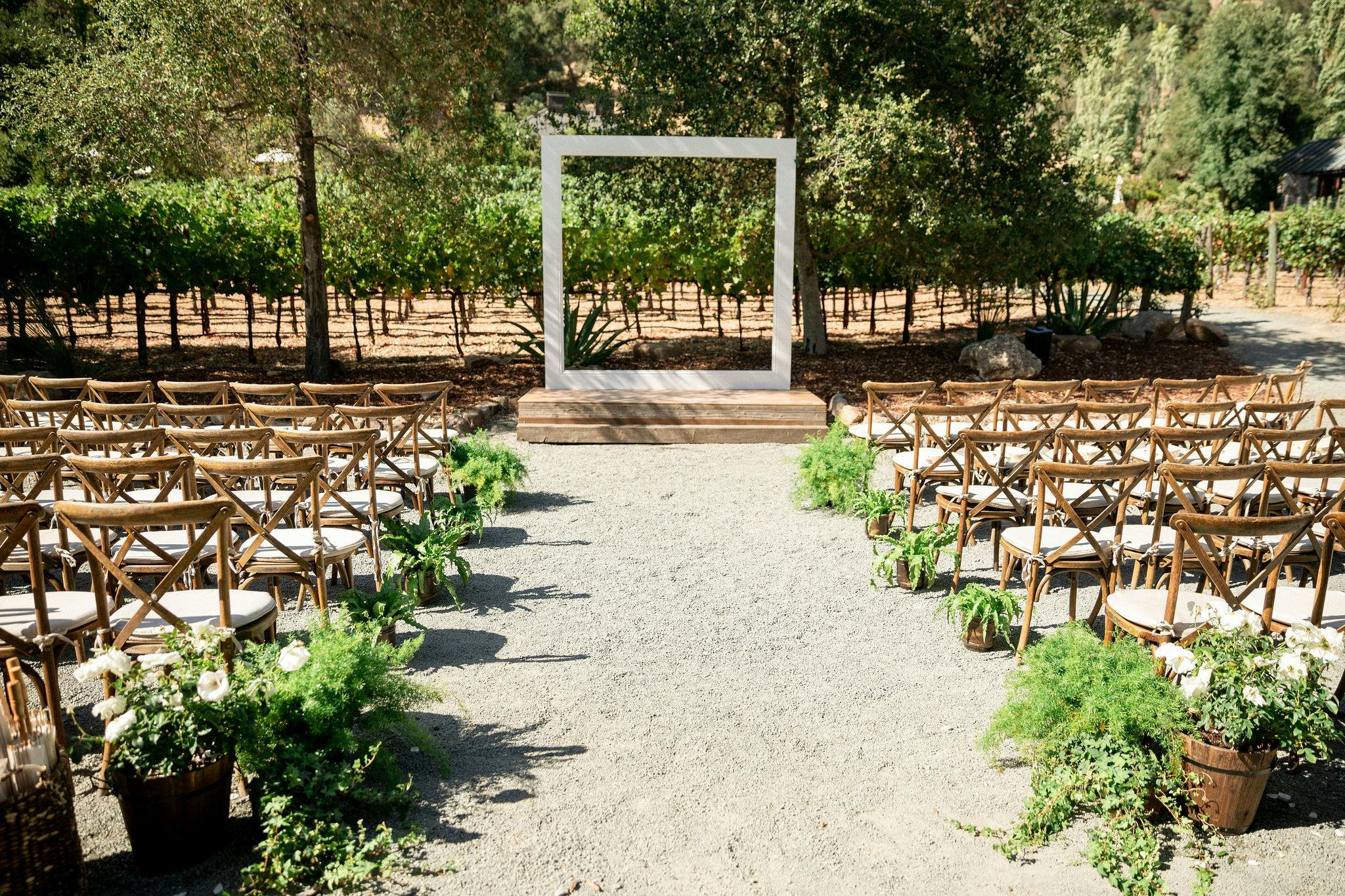 An outdoor wedding with wooden chairs and a square archway