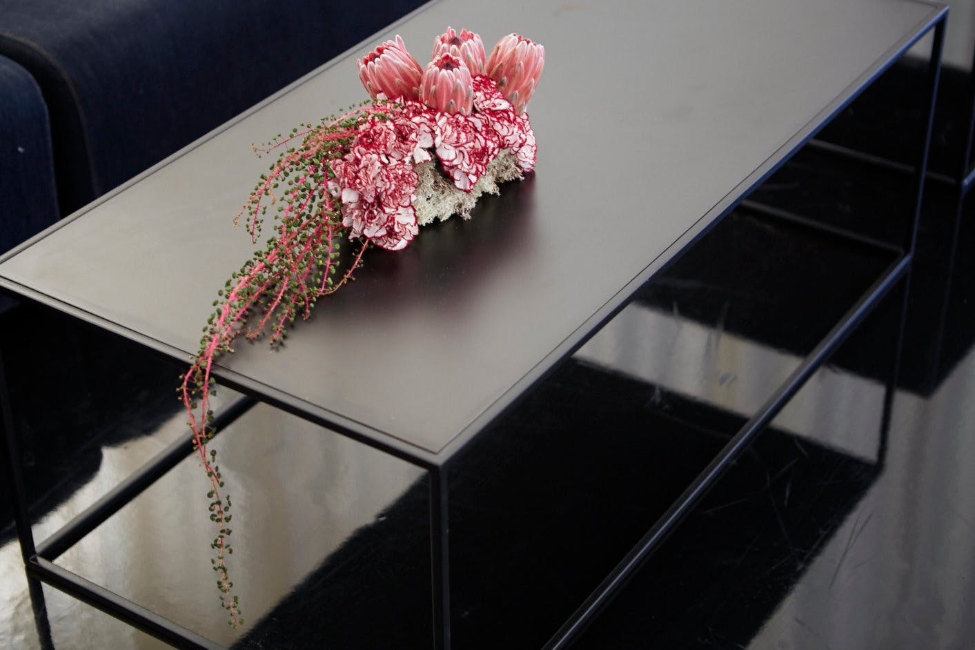 a sleek charcoal gray table holds a single arrangement of bright pink flowers. 