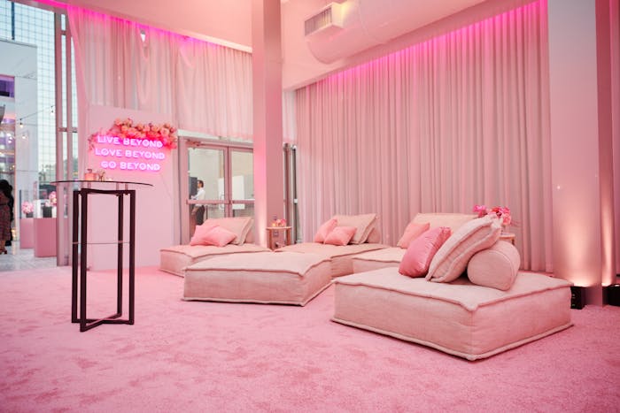 light pink couch poufs sit atop pink carpeting, pink draping and pink neon signs